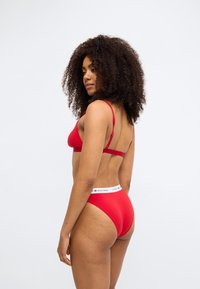 Rød bh og matchende trusse sæt lavet af blødt stof, med tynde stropper, lav ryg og en taljebånd med logo-detaljer.