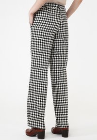 Pantalons à motif pied-de-poule noir et blanc, avec une coupe ample, des poches latérales et une taille mi-haute. Associés à des chaussures à talons bruns.