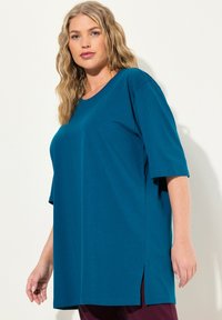 Türkisfarbenes, übergroßes T-Shirt aus weichem Stoff, mit Rundhalsausschnitt, kurzen Ärmeln und seitlichen Schlitzen für zusätzliche Bewegungsfreiheit.