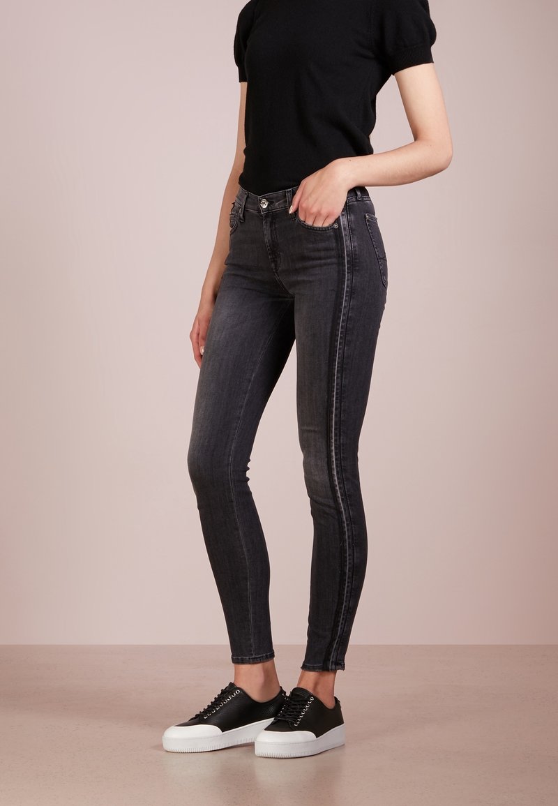 Czarne skinny jeans z przetarciami, wysoki stan i zdobienia po bokach, zestawione z czarnymi trampkami z białymi podeszwami.