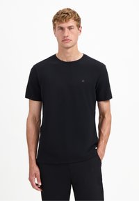 Zwarte korte mouwen t-shirt van textured stof met een ronde halslijn. Heeft een klein logo detail op de borst.