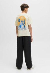 Camiseta de manga corta amarilla clara con un diseño gráfico azul de elementos de Mykonos y el texto "MYKONOS PURE PARADISE" en la parte posterior.