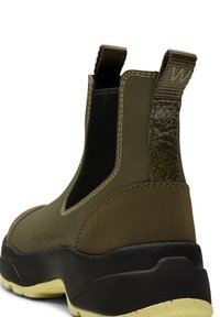 Botín impermeable en verde olivo con suela negra, paneles laterales elásticos, acento texturizado en la parte trasera y detalle de costura en contraste.