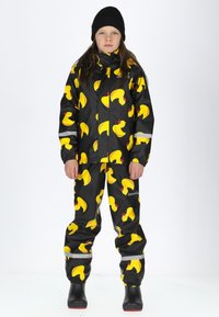 Schwarze Regenjacke und Hose mit gelbem Gummientenmuster, ausgestattet mit elastischen Bündchen und reflektierenden Streifen. Abgerundet mit schwarzen gummierten Stiefeln.
