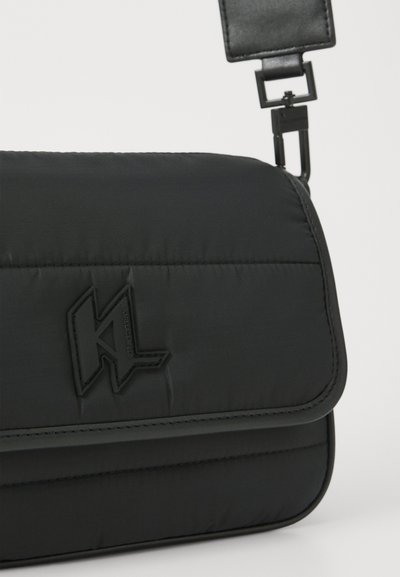 Sac bandoulière synthétique noir avec une finition rembourrée, présentant un logo en relief bien visible, une bandoulière réglable et un rabat.