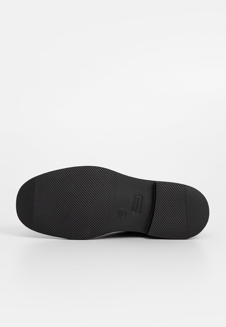 Suela de zapato negra con una superficie de goma texturizada, punta redonda y un borde liso. Incluye un detalle de logotipo cerca del talón.
