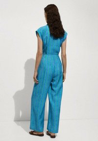 Jumpsuit a righe blu con maniche corte, vita aderente e pantaloni a gamba larga. Il tessuto ha una texture liscia e un motivo vivace.