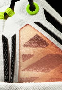 Buty sportowe z białą tekstylną cholewką z czarnymi akcentami, przezroczystą pomarańczową panelem wyświetlającym geometryczne wzory oraz neonowymi zielonymi elementami.