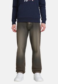 Jeans marroni scuri con una texture sbiadita, caratterizzati da una vestibilità standard e un motivo sottile. Indossati con una felpa blu navy e sneakers bianche.
