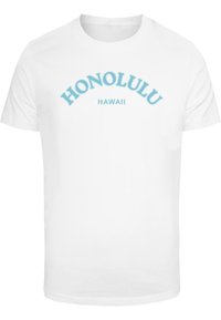 Balts kokvilnas T-krekls ar zilu viļņotu tekstu, kas lasāms "HONOLULU" un zem tā "HAWAI". Gluda tekstūra, klasiskā piegriezumā, īsas piedurknes.