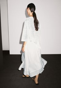 Helles blaues, fließendes Kleid mit einem strukturierten, locker gestrickten Oberteil und einem ausgestellten Rock, der am Saum horizontale Rippdetails aufweist. Paar schwarze Sandalen.