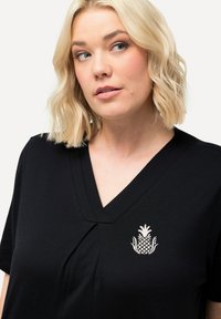 Svart V-ringat t-shirt med en plisserad design och en vit ananasbrodering på bröstet. Mjuk tyg med korta ärmar.