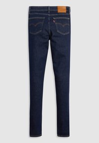 Jeans en denim bleu foncé avec une coupe fuselée. Les caractéristiques incluent des coutures dorées contrastantes, une patch en cuir beige à l'arrière et des poches arrière doubles.