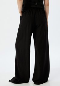 Schwarze weite Hose mit weicher Textur, elastischem Bund und Seitentaschen, in lockerem Schnitt bis zu den Knöcheln.