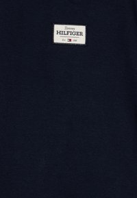 Maglietta di cotone blu navy con un'etichetta rettangolare bianca con testo nero che riporta "Tommy HILFIGER" e sotto "Est. 1985".