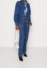 Jeansjacka med puffdetaljer på axlarna, kombinerad med högmidjade jeans. Modellen håller en vit handväska och bär svarta spetsiga klackar.