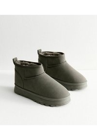 Botas de tobillo en ante sintético verde oliva, con un suave forro de pelaje, suela de goma flexible y una pestaña para ponerlas y quitarlas fácilmente.