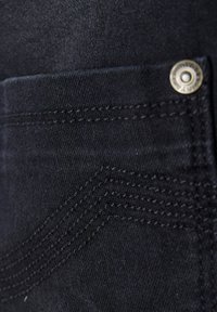 Svart denimstoff med nærbilde av en lomme. Viser synlige sømmer og en rund, gyllen metallknappdetalj.
