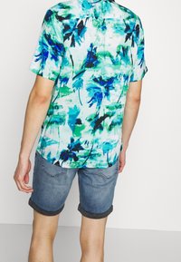 Koszula z krótkim rękawem w niebiesko-zielony tropikalny wzór, wykonana z lekkiego materiału. Połączona z dżinsowymi szortami z podwiniętymi mankietami i dwoma tylnymi kieszeniami.