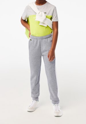 Grünes und graues Color-Block-T-Shirt mit einem weißen Logo, kombiniert mit grauen Joggern mit weißen Seitenstreifen und elastischem Bund, getragen mit weißen Sneakern.