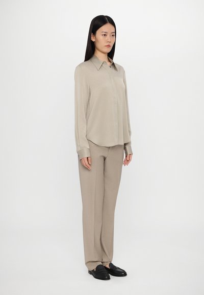 Beige button-up shirt with a pointed collar, paired with matching beige trousers. The outfit features a loose fit and smooth texture. Black shoes complete the look.