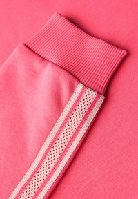 Tessuto di felpa rosa con polsini a costine e una striscia laterale caratterizzata da un motivo testurizzato in una tonalità più chiara. Texture complessivamente morbida e liscia.