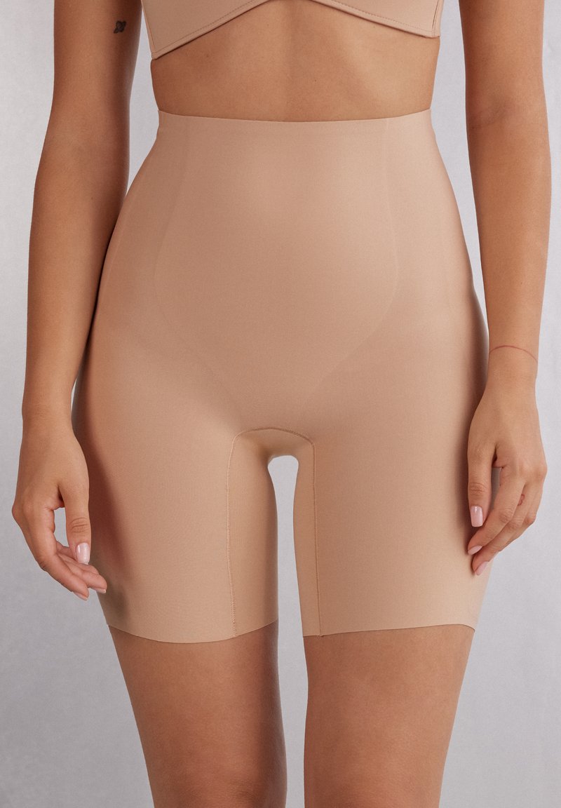 Beige hoog-getailleerde shaping shorts gemaakt van een gladde, rekbare stof. Kenmerkt zich door een lengte tot halverwege de dij met een naadloos ontwerp en geen zichtbare naden.