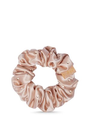 Beige Satin-Haargummi, dekoriert mit kleinen Perlen und einem Stoffetikett mit goldener Schrift auf weißem Hintergrund.