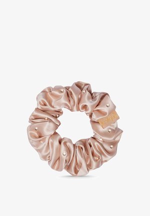 Chouchou en satin beige décoré de petites perles et d'une étiquette en tissu avec inscription dorée sur fond blanc.