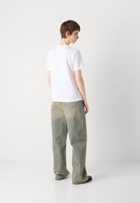 Hvit bomulls T-skjorte med rund hals, sammen med lyseblå bred ben-jeans som viser en falmet, slitt tekstur og to baklommer.