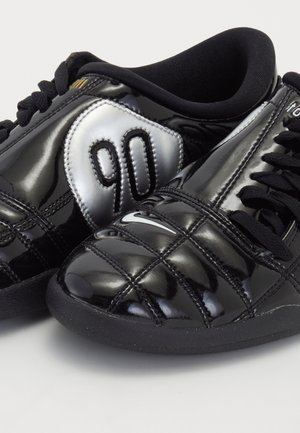 Par sorte lavtop Nike sportsko med hvide Swoosh-logoer og "90" detalje på ydersiden, vist på en ensartet lys baggrund.
