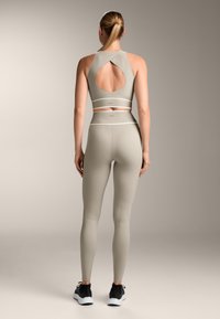 Világosszürke sportos öltözet, amely magában foglal egy nyitott hátú sportmelltartót és magas derekú leggingset, sima, rugalmas anyagból készült.