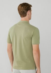 Olivgrön piké med kort ärm, med en klassisk krage och sidsprund för ökad rörelsefrihet. Len bomullstyg.