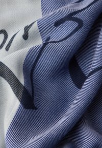 Gros plan sur un tissu bleu et blanc avec un fin nervurage diagonal et un texte imprimé noir partiel, montrant des plis et des détails de texture.