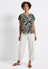 Short-sleeve green and white zebra-patterned blouse with a v-neck, paired with cream wide-leg pants and brown flat sandals.