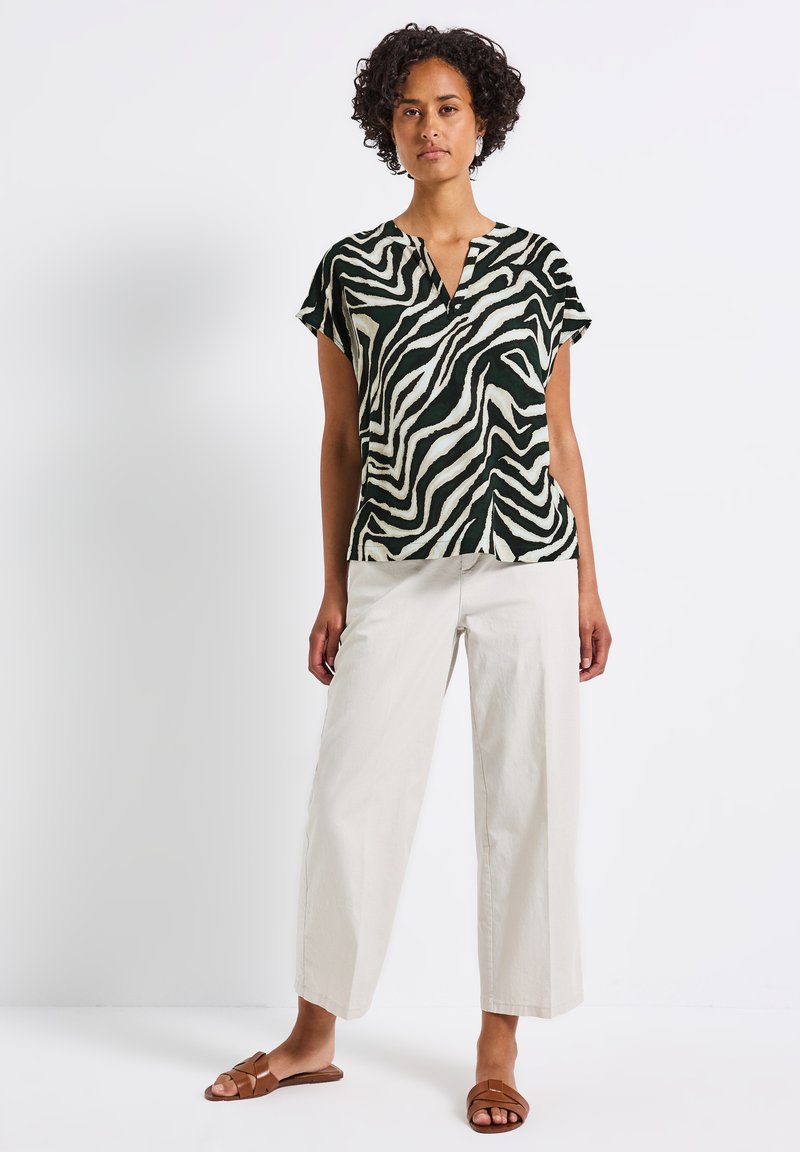 Short-sleeve green and white zebra-patterned blouse with a v-neck, paired with cream wide-leg pants and brown flat sandals.