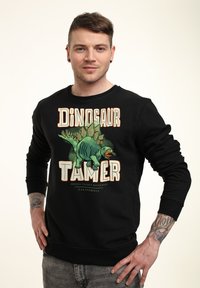 Felpa nera a maniche lunghe, con una grafica di un dinosauro e il testo "DOMATORE DI DINOSAURI" in caratteri spessi e colorati.