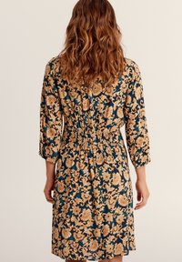 Abito con motivo floreale nei colori blu e oro, maniche a tre quarti, vita arricciata e vestibilità comoda, che mette in mostra disegni intricati.