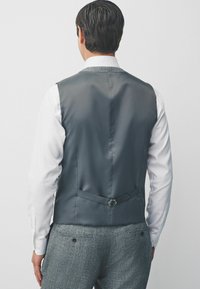 Graues Satin-Westen mit glatter Textur, ausgestattet mit einer verstellbaren Schnalle am Rücken und einem kontrastierenden hellen Hemd. Taillierter Schnitt und sauberes Design.