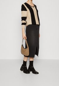 Czarny i beżowy sweter w paski, szara spódnica dżinsowa z przednim rozcięciem, brązowa torba na ramię, czarne buty na obcasie typu block heel, prążkowane czarne skarpetki.