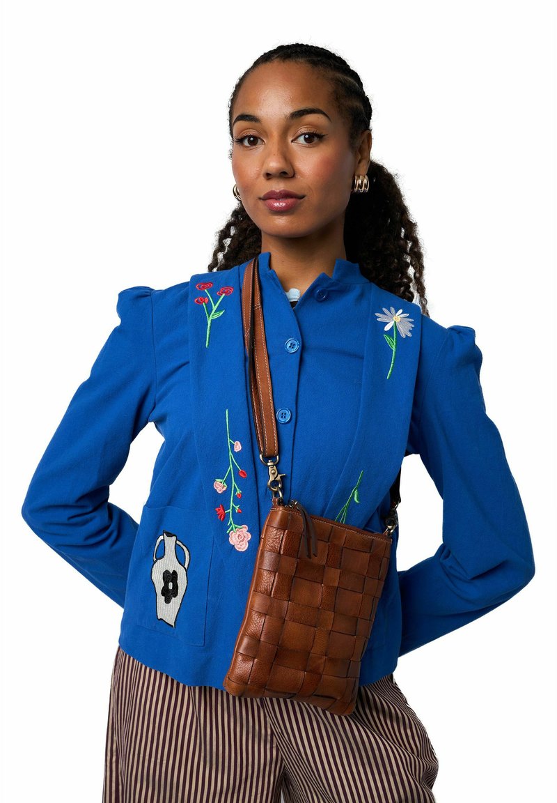 Veste tissée bleu vif avec broderie florale et boutons ; sac bandoulière en cuir tressé marron ; pantalon à rayures verticales.