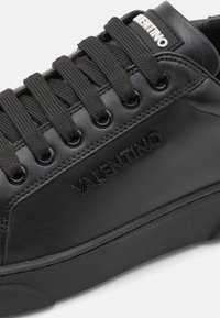 Baskets en cuir noir avec surface texturée, lacets plats et logo "VALENTINO" embossé sur le côté. Semelle en caoutchouc et œillets en métal.