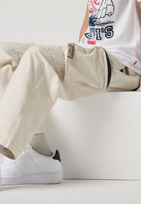 Beiga cargobyxor med en sidodragkedjeficka och subtila sömdetaljer, parat med vita sneakers med en svart hälaccent.