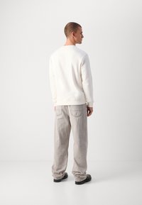 White sweatshirt with a straight fit, crew neckline, and ribbed cuffs, paired with light gray, loose-fit jeans featuring back pockets.