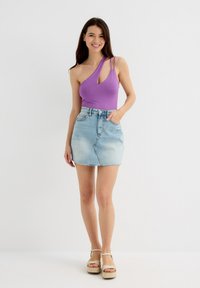 Bodysuit morado de un solo hombro con un corte en forma de llave, combinado con una mini falda de mezclilla azul clara. Llevado con sandalias de plataforma beige.