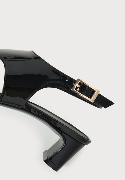 Μαύρο παπούτσι slingback από λουστρίνι με χαμηλό τακούνι και χρυσή αγκράφα σε λευκό φόντο.