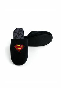 Pantofole in peluche nere con il logo di Superman rosso e giallo sulla parte anteriore. La soletta interna grigia presenta un motivo a ripetizione con il logo di Superman.