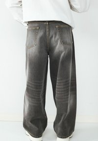 Weit geschnittene Jeans aus dunkelgrauem Denim mit verwaschenem Finish, zwei Gesäßtaschen und einer leicht abgenutzten Textur entlang der Seiten.