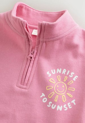 Lyserød fleece-trøje med lynlåslukning ved kraven. Har et legende solmotiv og teksten "SUNRISE TO SUNSET" i hvidt og gult.