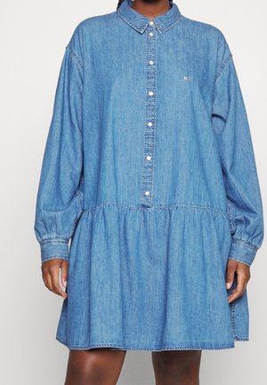 Lässig geschnittenes, langärmliges Denim-Kleid mit Perlenknöpfen und gerafftem Rock, getragen von einer dunkelhäutigen Person vor einem schlichten Hintergrund.